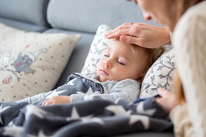 a sleeping child in bed while his mom puts her hand on his head